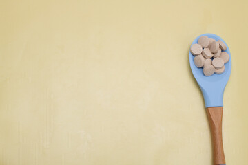 Vitamins in a blue spoon on yellow background. with space for text
