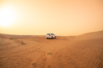 Fototapeta na wymiar SUV truck parked on a sand dune near Dubai, UAE, sunset sky in the background. Extreme sports, adventure and travel concept. Wide angle shot.