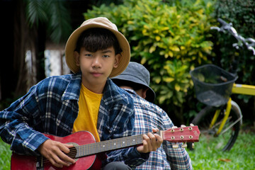 Asian boy is playing acoustic guitar in the schoolpark with his friend happily, soft and selective...