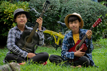 Asian boy is playing acoustic guitar in the schoolpark with his friend happily, soft and selective focus, concept for happiness of children with popular instruments around the world.