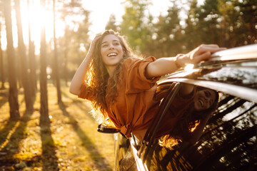 Happy woman in a car catches the wind from the car window, enjoying nature. Young woman on a car...