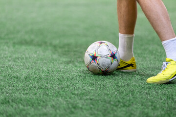 Football Futsal ball and man player legs on artificial grass field indoors.