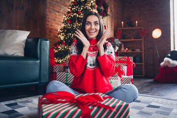 Portrait of excited shocked cheerful girl sitting on floor raising hands rejoicing unexpected gift...
