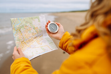 A young woman traveler with a compass and a map in her hands, reading a map looking for directions on the beach near the sea. Adventure, vacation concept. Active lifestyle. © maxbelchenko