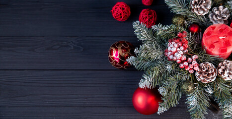 Christmas decor, fir branches, red balls, candle, rattan balls, cones, red berries in hoarfrost. On a dark background with copy space. Holiday mood.