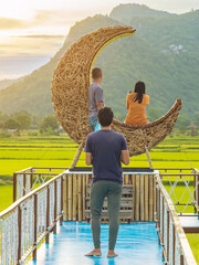 Man using camera to take photo with happiness young couple on crescent moon chair made of rattan in...