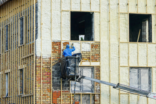 Technician spraying thermal insulation foam layer on the exterior wall using plural component gun for polyurethane foam