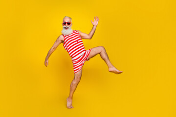 Fototapeta na wymiar Full length photo of impressed funny senior man wear red striped swimsuit having fun walking dancing isolated yellow color background