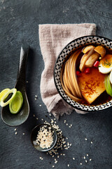 Asian soup with egg, tofu, mushrooms and onion on black background. Traditional food concept.