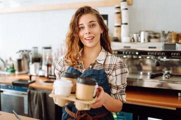 Female barista holding disposable takeaway cups. The young barista owner behind the bar gives out...
