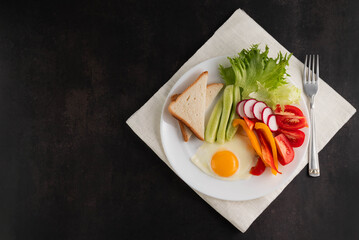 On a white plate there are fried eggs and fresh vegetables and toast. The concept of proper nutrition.