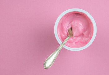 Strawberry pink yogurt in small plastic cup with little spoon isolated on pink background with copy...