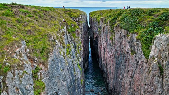 Tourists climbing the mountain rocky formation at Huntsman's Leap in Wales. Stunning panoramic sea views with a cliff gap near Saint Govan's Chapel on the cliffside.