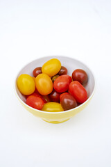 Colorful cherry tomatoes in a jellow bowl. Fresh, ripe type of small and round cocktail tomatoes, of red, yellow and orange color. Solanum lycopersicum var. cerasiforme. Isolated, close up, from above