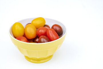 Colorful cherry tomatoes in a jellow bowl. Fresh, ripe type of small and round cocktail tomatoes, of red, yellow and orange color. Solanum lycopersicum var. cerasiforme. Isolated, close up, from above