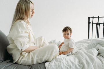 Happy mother plays with her child while sitting in bed, in the morning.