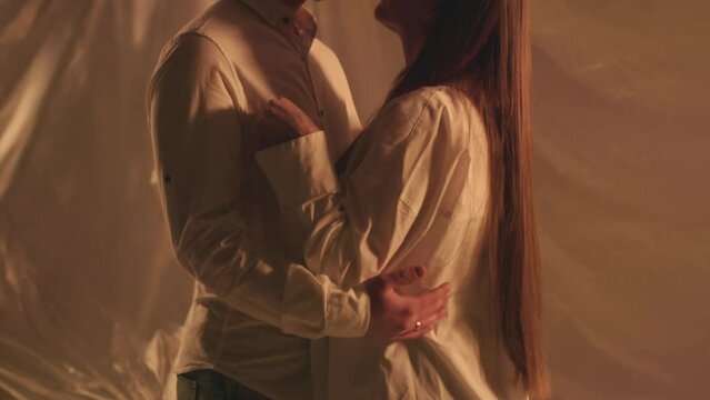 Slo motion of hugging couple in studio turning off light on background. Young boyfriend sensual cuddles with girlfriend indoors. Romantic couple wearing white clothing for anniversary shot