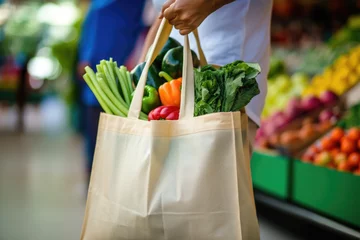  Close-up shot of a person's hand holding a eco friendly reusable shopping bag with bio vegetables at a local farmers market. Healthy food shopping, zero waste, plastic free © Jasmina