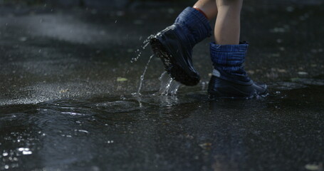 Child feet walking in the rain outside in city street sidewalk with water droplets falling in super...