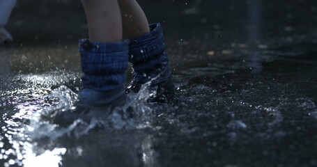 Child stepping in water puddle in super slow-motion wearing rainboots splashing liquid droplets...