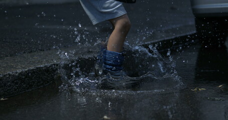 Child jumping into puddle in the street with rainboots in super slow-motion at 800 fps captured in high-speed, splashing water everywhere