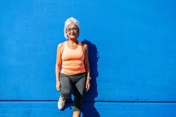 Senior sportive woman leaning on a blue wall