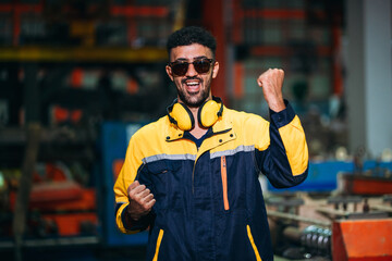 Portrait of happy industrial worker looking camera at factory machines. Technician working in metal sheet at industry.