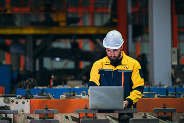 Industrial worker inspecting with labtop machine at factory machines. Technician working in the metal sheet company.