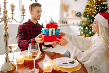 Beautiful couple in love near the Christmas tree, celebrating the exchange of gifts, spending time together. Holiday concept.