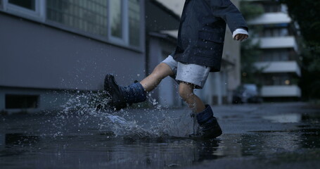 Nostalgic scene of child kicking puddle of water in street alley having fun by himself filmed in high-speed camera
