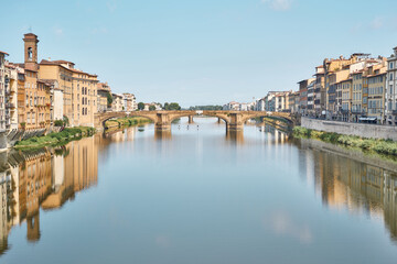 Fototapeta na wymiar Santa Trinità bridge, seen from Ponte Vecchio, on a summer day with blue sky and reflections on the Arno