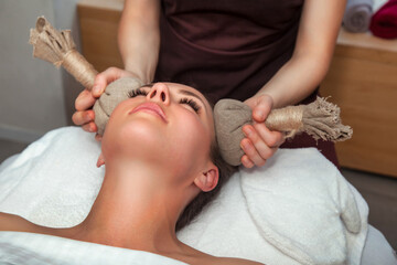Thai herbal massage with bags head for lady patient in beauty SPA, medic cosmetic therapy closeup....