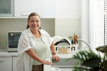 Portrait of smiling senior woman standing at kitchen sink