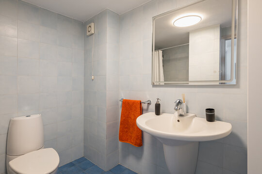 Mirror over sink and toilet bowl in tiled modern bathroom