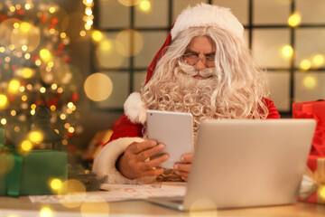 Fototapeta na wymiar Santa Claus using tablet computer at home on Christmas eve