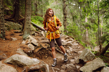 Smiling woman traveler along a forest hiking trail in the mountains against the backdrop of nature....