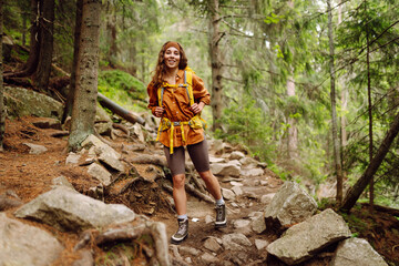 Smiling woman traveler along a forest hiking trail in the mountains against the backdrop of nature. Young woman with backpack traveling outdoors. Hiking, active lifestyle.
