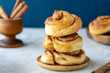 Heap of cinnamon rolls on a wooden plate over linen tablecloth with dark blue background, cinnamon...