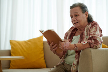 Elderly woman reading captivating book at home