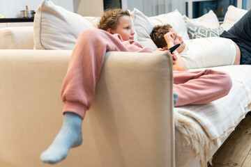 Children  lying on the sofa and watching TV interesting cartoon. A girl holding TV remote. Rest in the evening. 