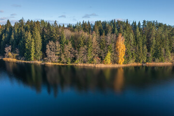 View on picturesque bank of lake in autumn morning, Lake Bolduk. Small wooden piers on the right bank of the lake. The woods is reflected into the water of lake by dark colors.