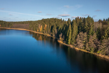 Fototapeta na wymiar Aerial view on bank lake Bolduk in the autumn sunny morning. Woodland and sky are reflected on the water of lake. Small wooden piers on the right bank of the lake.