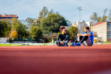 Young fitness couple resting after exercising outdoors, sitting on running track.