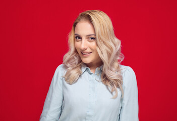 Smiling young woman, brown eyes and blond hair, head and shoulders portrait concept, isolated on red background. Pretty girl with laugh expression.