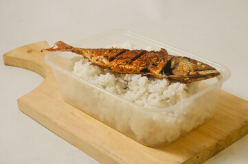 White rice and a fried fish served in a plastic box on a wooden cutting board isolated on a white...