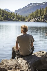 Fototapeta premium A man sitting on rocks admiring a beautiful lake