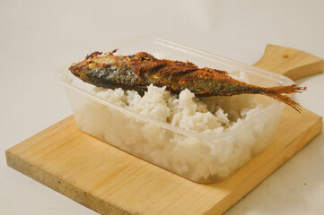 White rice and a fried fish served in a plastic box on a wooden cutting board isolated on a white background