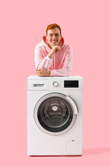 Young man near washing machine on pink background