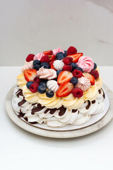 Pavlova cake with whipped cream cheese, chocolate sauce, fresh berries and meringues on plain background