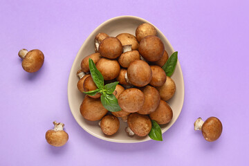 Plate with fresh mushrooms and basil on lilac background